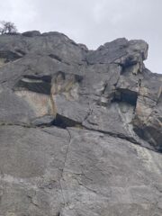 La parete vista dalla base. Al centro la fessurina di L1, la nicchia di sosta, il diedro giallo di L2. Sulla destra il sistema di fessurini della variante 