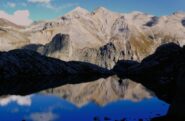 In discesa, il lago Niera in ombra si illumina con le cime dietro Rocca Castello